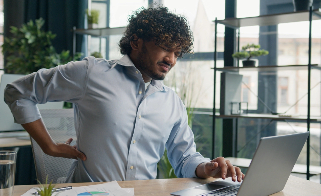 A man at his laptop holding his back in pain