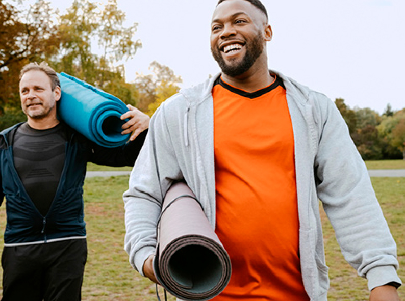 2 people carrying yoga mats in a park